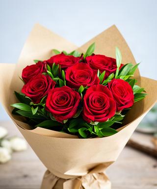 Ramo compacto de rosas rojas con follaje verde y envoltorio de papel natural
